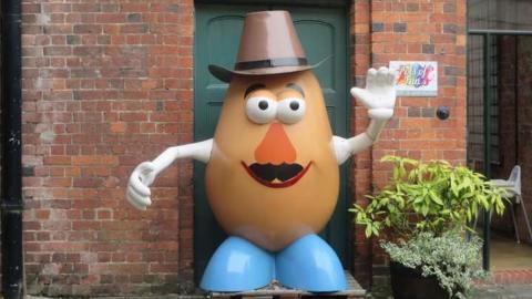 A large statue of the children's toy, Mr Potato Head, stood outside a brick building with a green door.
