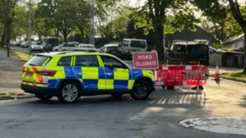 A police car sits ahead of a road closed sign on the road