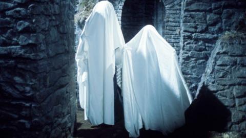 Two people in a castle wearing sheets over themselves to look like ghosts.