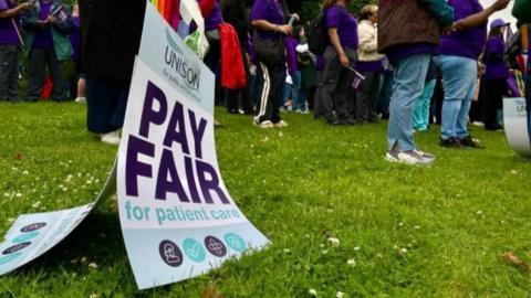 A sign reading 'Pay Fair for pateint care' on the floor by a staff picket lines feet