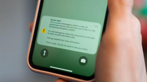 Image of a hand holding a phone. On the phone reads an emergency alert: "Severe alert. This is a test of Emergency Alerts, a new UK government service that will warn you if there's a life-threatening emergency nearby. In a real emergency, follow the instructions in the alert to keep yourself and others safe. Visit gov.uk/alerts for more information. This is a test. You do not need to take any action."