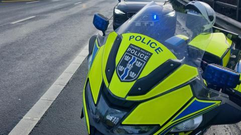 A motorbike used by roads policing officers is parked on the side of a road. The photo shows the high visibility graphics on the front of the windscreen with the Thames Valley Police logo in the middle.