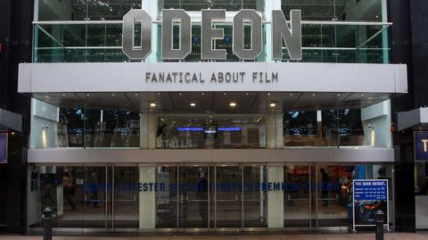 The entrance to the Odeon cinema in London's Leicester Square. It has glass doors and walls and says Fanatical About Film under the Odeon sign.