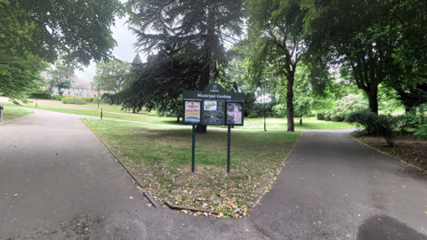 A sign on the entrance to Municipal Gardens, which is a green park with lots of trees.