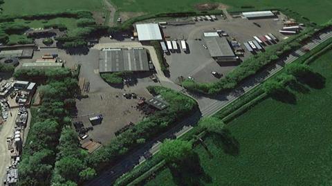 The land at Hilltop Farm from a bird's eye view. There are a number of buildings and concrete hardstanding on the site, with a road separating it from a field 