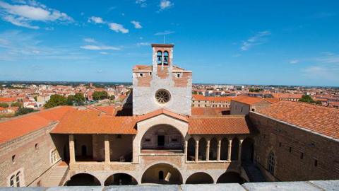 General view of Perpignan, with a church clock tower overlooking the city against a blue sky.