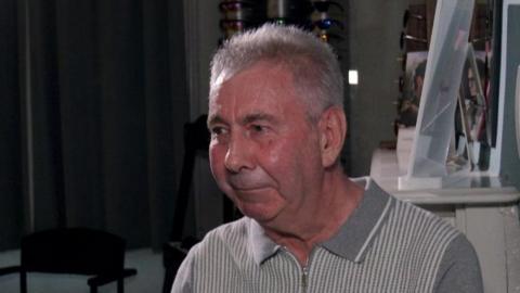 Robert Campbell looking to the side of the camera at the opticians, wearing a grey t-shirt and has grey hair.