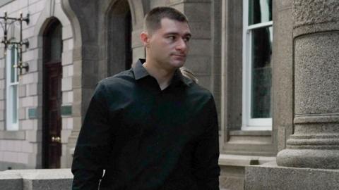 Artur Sevash-Zade walks into Jersey Royal Court. He is wearing a black shirt. He has short black hair.
