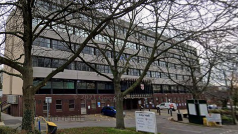 A view of Lincoln Hall from the road taken during the winter as the trees in front of the building are bare. The building is long and rectangular and has six floors.