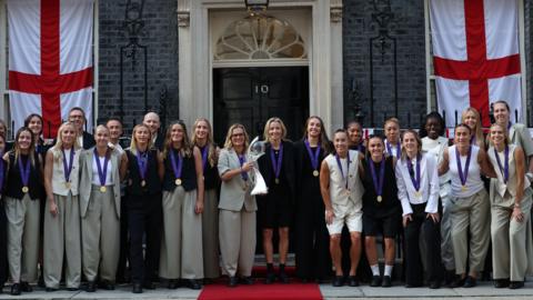 The England squad standing outside number 10 downing street while holding the euro 2025 trophy