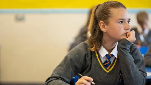 A pupil listens during a history lesson at Whitchurch High School on September 14, 2021 in Cardiff, Wales. The teenager is wearing a grey jumper, with a white shirt and blue and orange striped tie. 