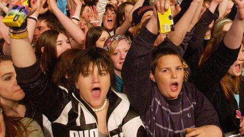 Yong people cheer in a crowd while holding yellow cameras