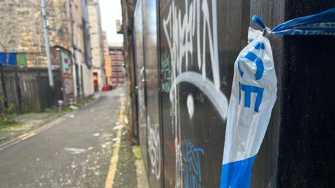 A close up of some blue and white police crime scene tape attached to a wall in Sauchiehall Lane