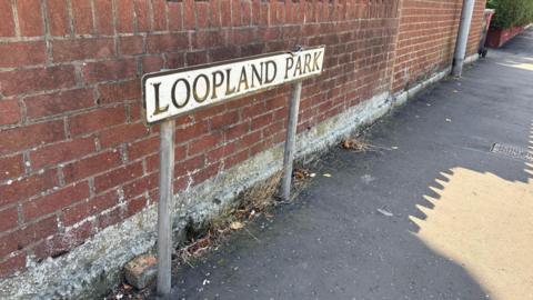 A red brick wall with a road sign reading "Loopland Park" in front of it. 