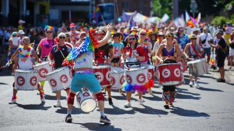 People at Bristol Pride 2025 marching through the street with marching drums and wearing colourful outfits.