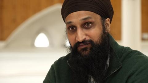Harjit Singh, a man with a black beard wearing a black fleece and turban, is pictured facing the camera.