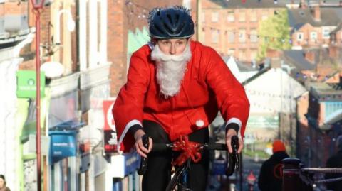 A woman in a Santa costume riding a bicycle