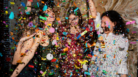 Girls dance and rejoice at a venue as a flurry of glitter and colourful confetti fall to the floor.