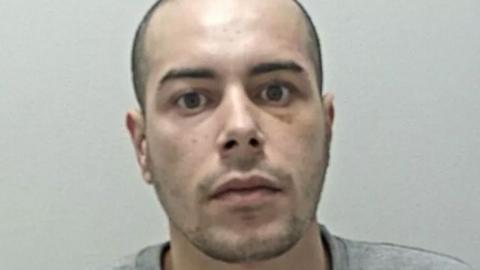 Mohammed Alshafi's mugshot. He has shaved dark hair and stubble and is wearing a grey sweatshirt