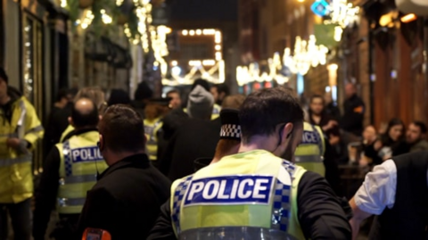 A large number of police officers in high-vis vests are among a crowd of people in a street at night. 