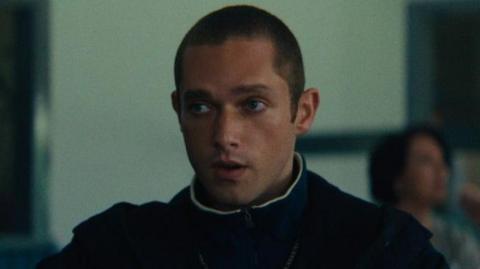 Sonny Walker, who is playing the role of Paul in Legends, is staring off camera in this still from filming. He has a buzz cut and is wearing a jumper with a coat over the top. 