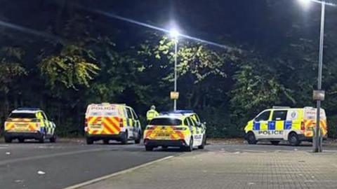 Five police vehicles in a car park in front of some trees