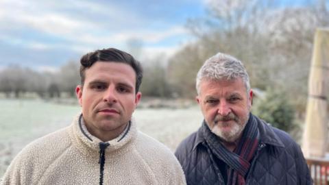 A man and his son stand outside their house in winter clothes. 