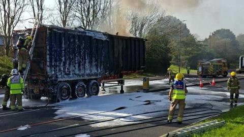 Lorry trailer with metal container on it covered in foam after being on fire.