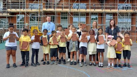 Teachers and children looking at the camera holding their decorated tiles.