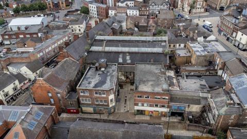 An aerial view of a town with an old indoor market building in the centre of the frame.