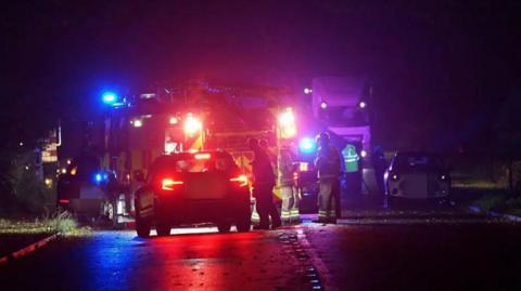 A picture of the scene where the crash happened, at night, with police and fire engines parked on the road