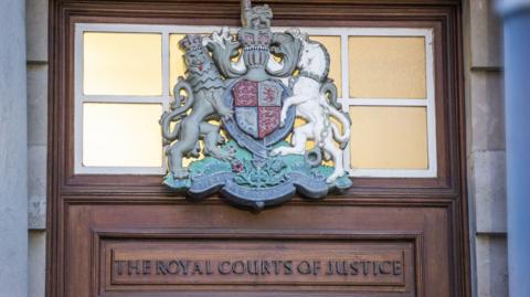 A brown door with an insignia. On the top of the door the words 'The Royal Courts of Justice'