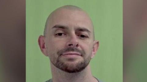 Jamie Smith, a man who is bald with brown stubble, in front of a green background.