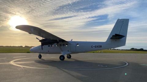 Aurigny's Twin Otter aircraft on the runway. It is white and is lit up by bright sunlight. 