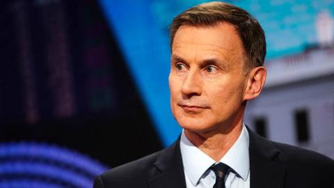 Jeremy Hunt looks away from camera wearing a suit and tie during a TV interview in April