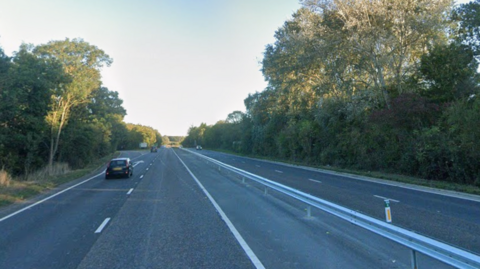 An empty dual carriageway with one car. There are trees on either side. 