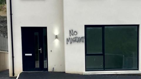 The front of a new build house In Londonderry with graffiti saying 'no migrants' and 'no scum' spray painted on the walls