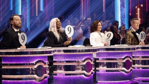 The Strictly Come Dancing judges holding up result boards of 9, 9, 9 and 10 in the Strictly studio.