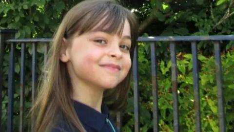 Saffie-Rose Roussos smiling for a picture next to some railings outside. 