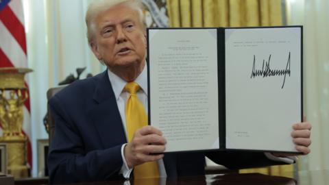 US President Donald Trump holds up a signed document