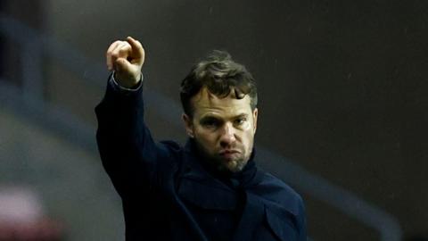 Plymouth Argyle boss Tom Cleverley pointing towards his players from the touchline with his right hand while pursing his lips together.