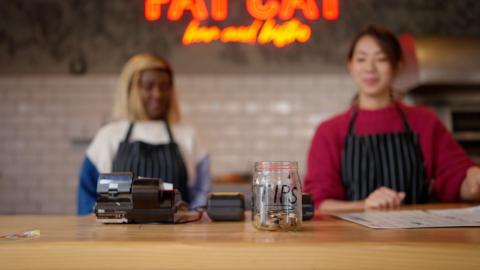 Two staff members who stand in front of a tip jar