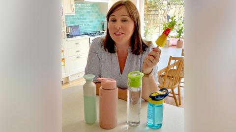 Catherine Burne holds an ice lolly in a kitchen with water bottles