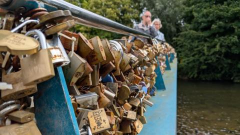 Hundred of padlocks on a blue bridge. A couple walk over the top