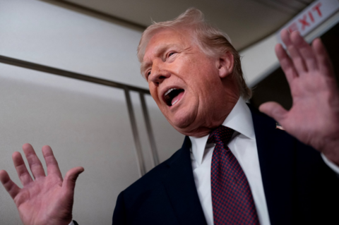 US President Donald Trump wearing a dark suit, white shirt and blue tie with red dots gestures with his hands as he speaks on Air Force One