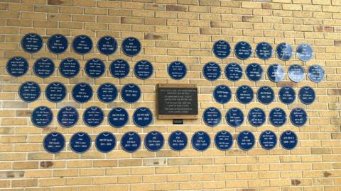 More than 50 blue memorial plaques on a brick wall, as a memorial for previous police dogs