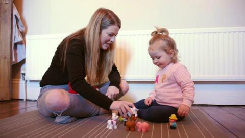 Mother and daughter play with farm animal toys in the living room