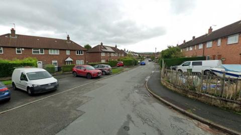 A street view image of a road in the middle of a residential estate. 