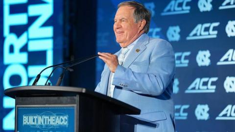 Bill Belichick speaking at a podium before the start of the US College season