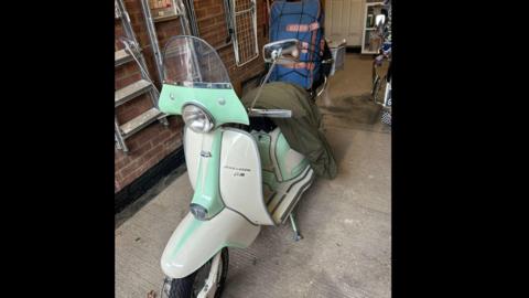 A cream 1963 Lambretta, with cyan markings, parked inside a garage.